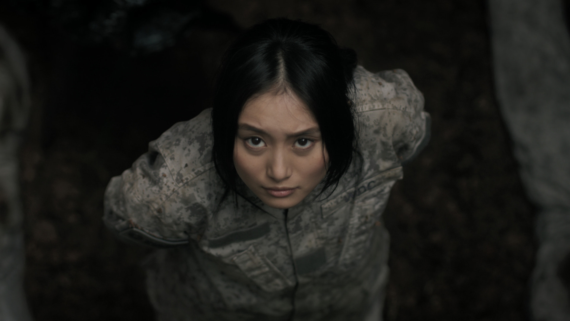 A woman in a soldier's uniform looks up from a hole