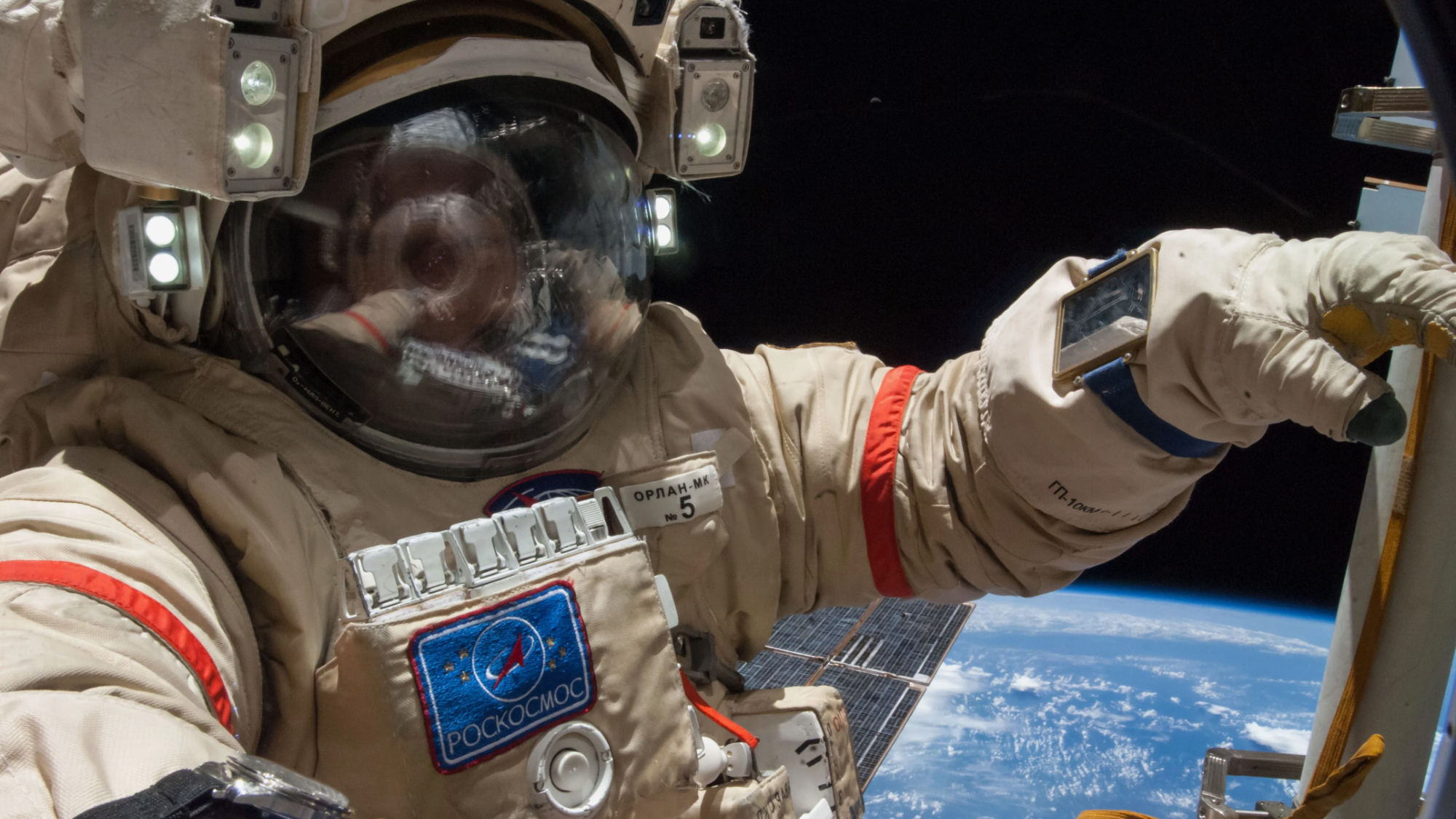 closeup of a spacewalking astronaut's helmet and torso, with earth in the background