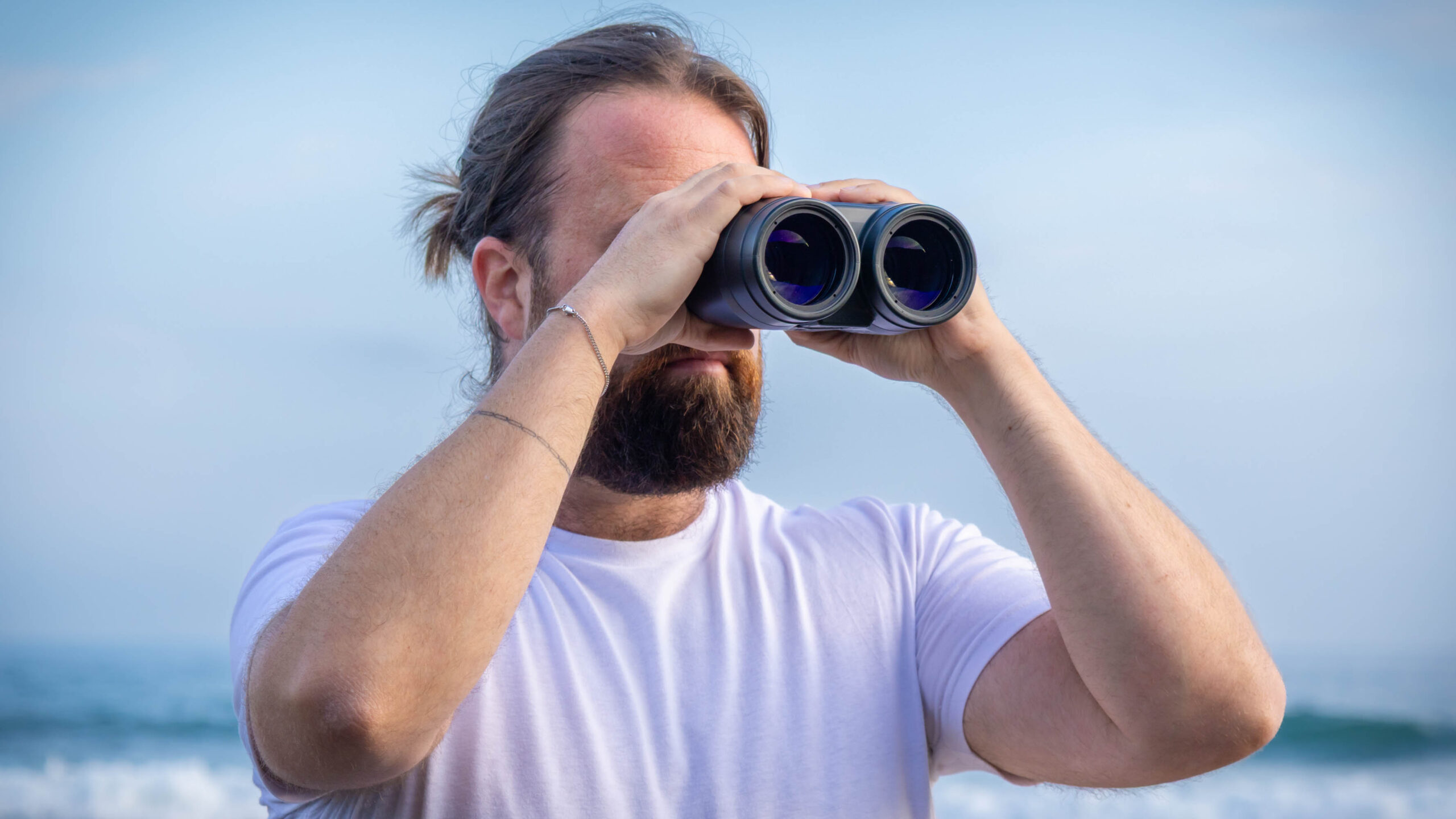 A male using the Canon 18x50 IS binoculars with the sea behind them.