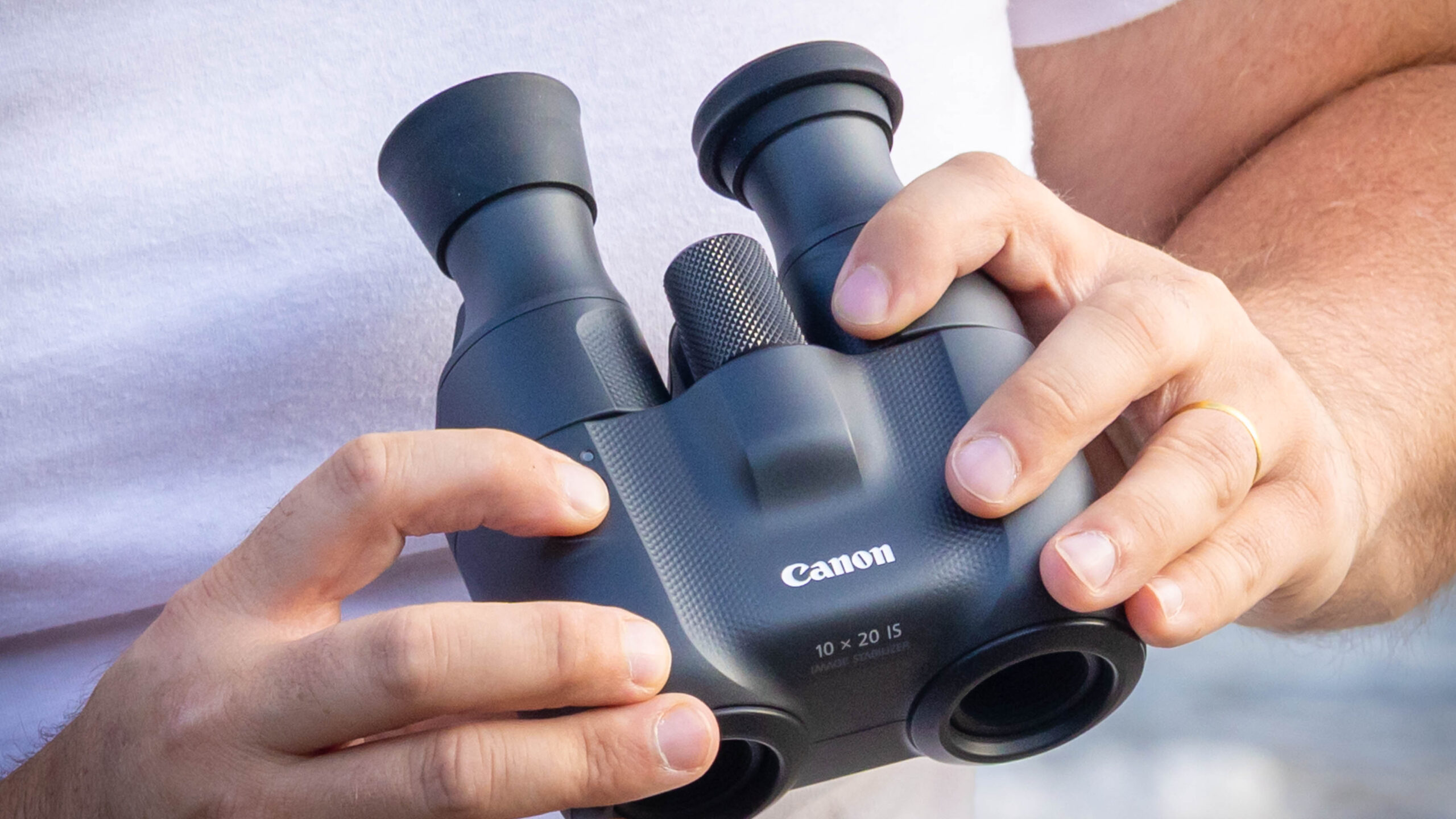 An extreme close-up of the Canon 10x20 IS binoculars being held in someone's hands.