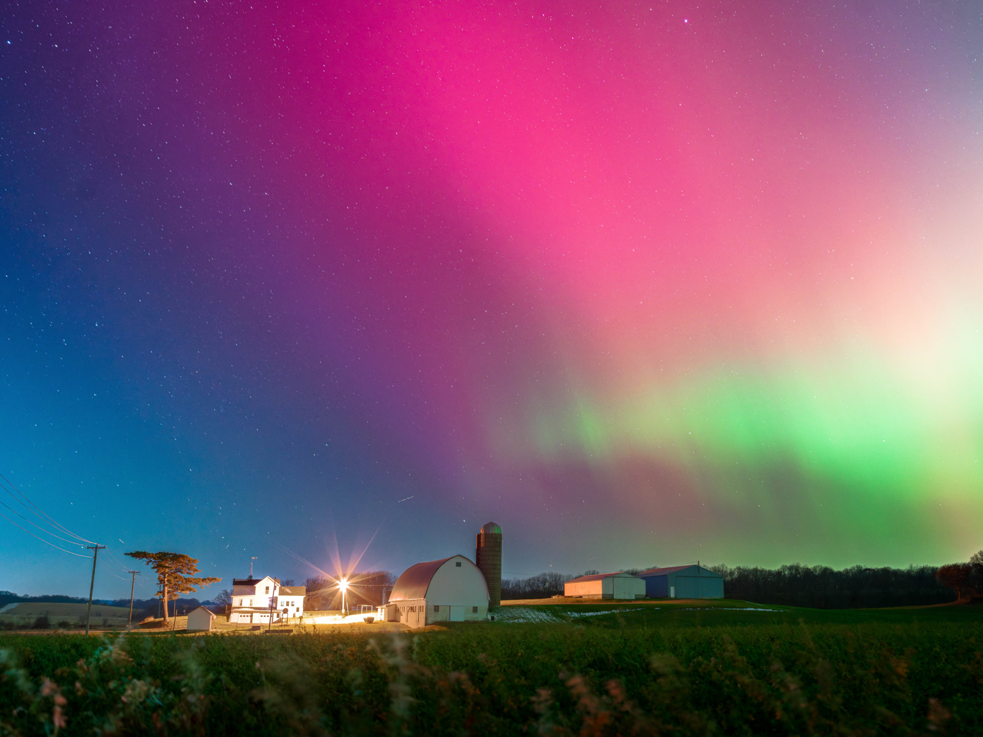 pink and green auroras dance over farm buildings.