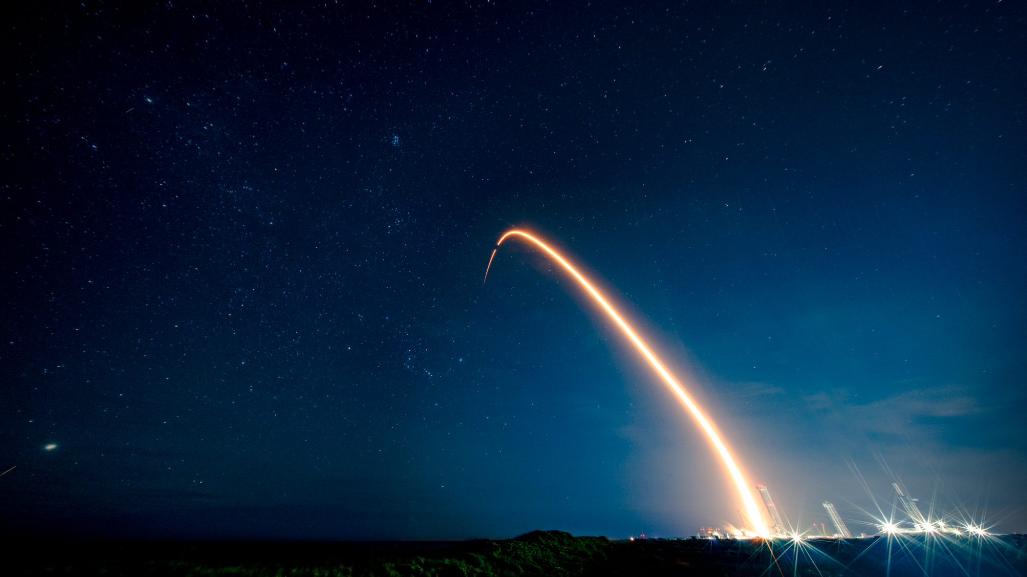 A rocket launch carves an orange arc into a dark night sky in this long-exposure photo.