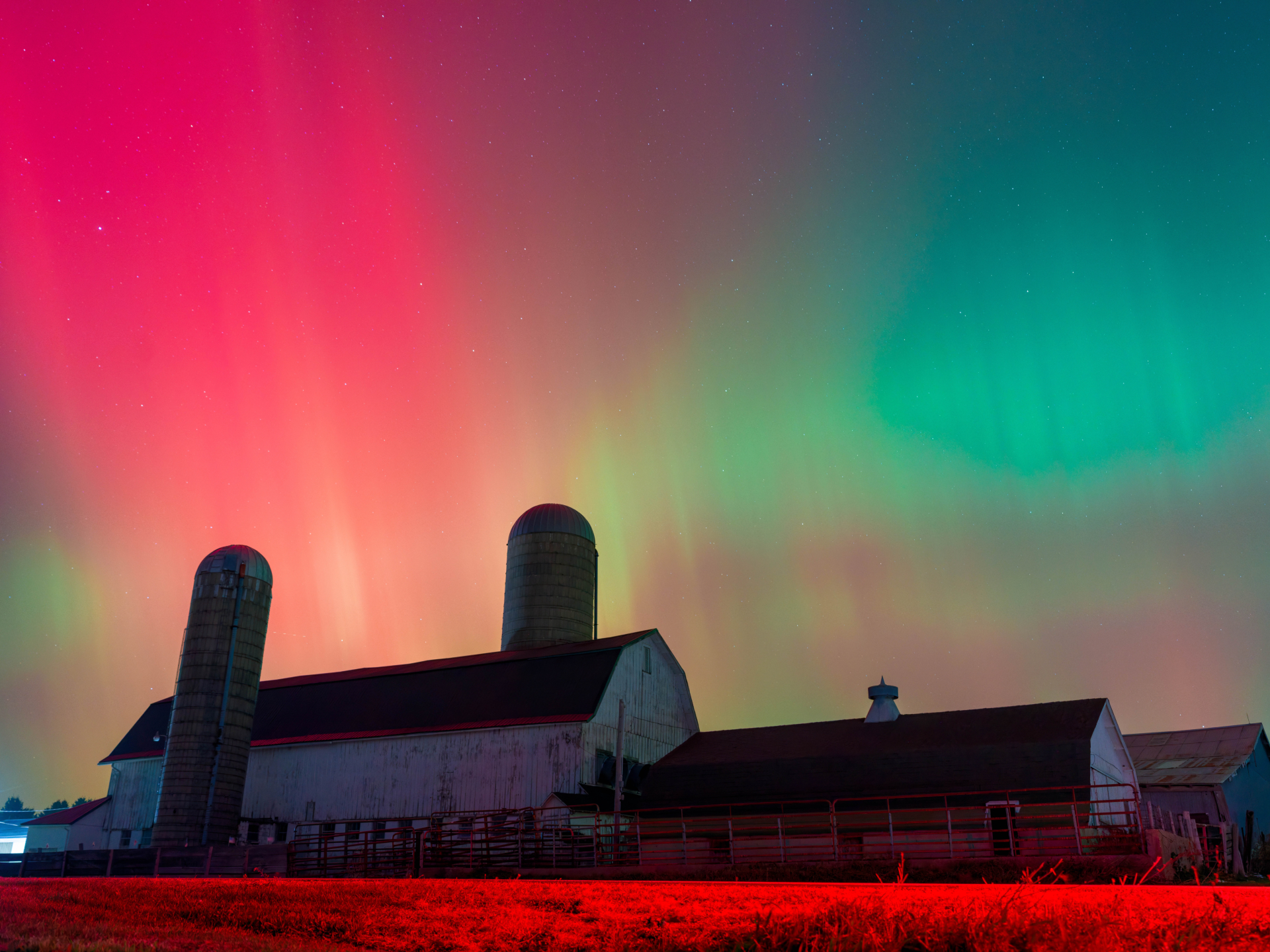 red and green aurora light over a farm building in the foreground.