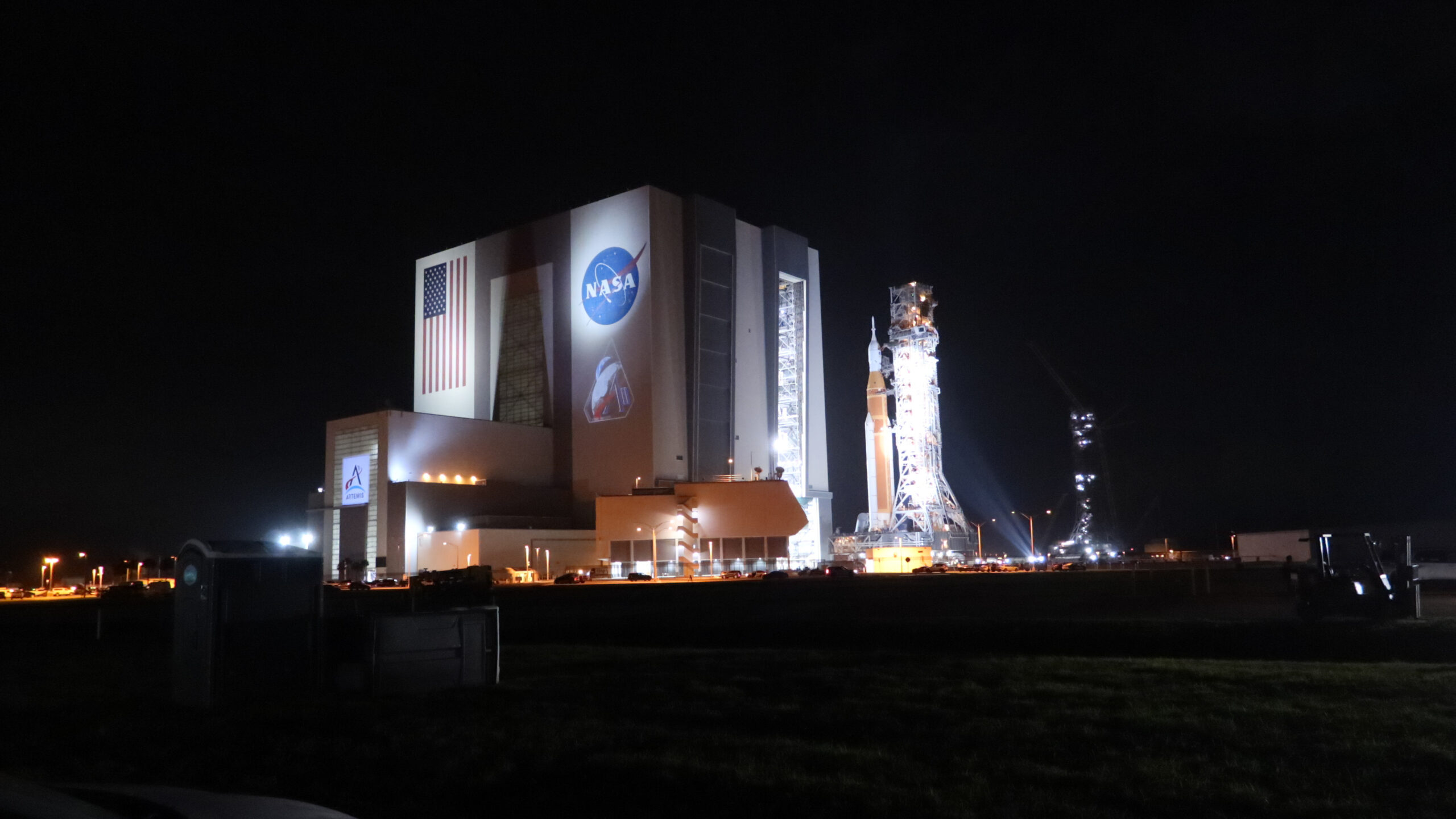 a large orange rocket emerges vertically from a giant grayish-white building at night