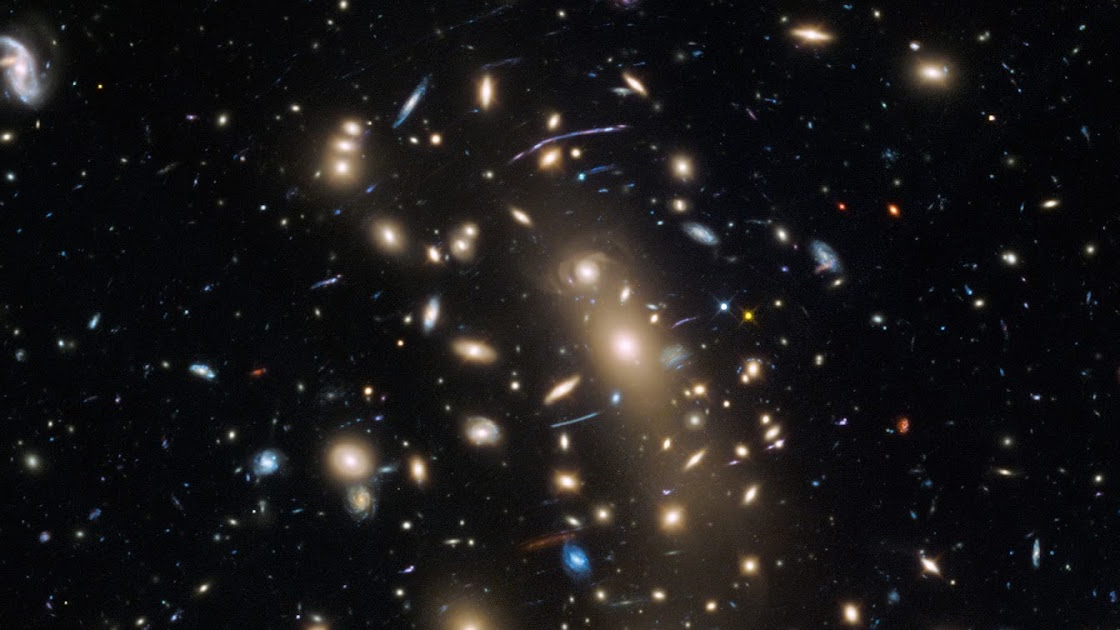 hubble telescope view of a galaxy cluster showing hundreds of galaxies in deep space, each of which looks like a small, bright disk