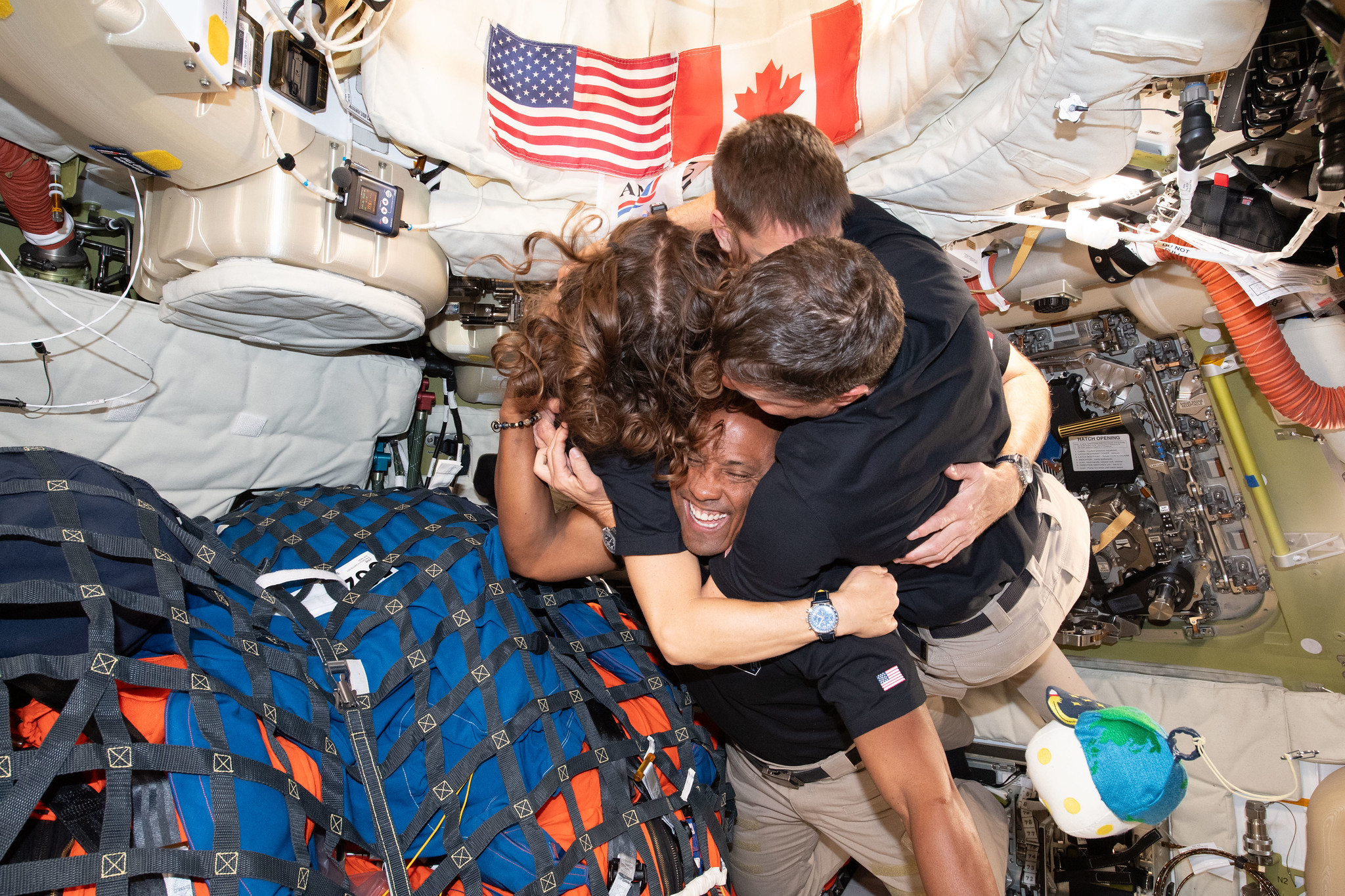 Four astronauts hug as they float in microgravity in a space capsule.