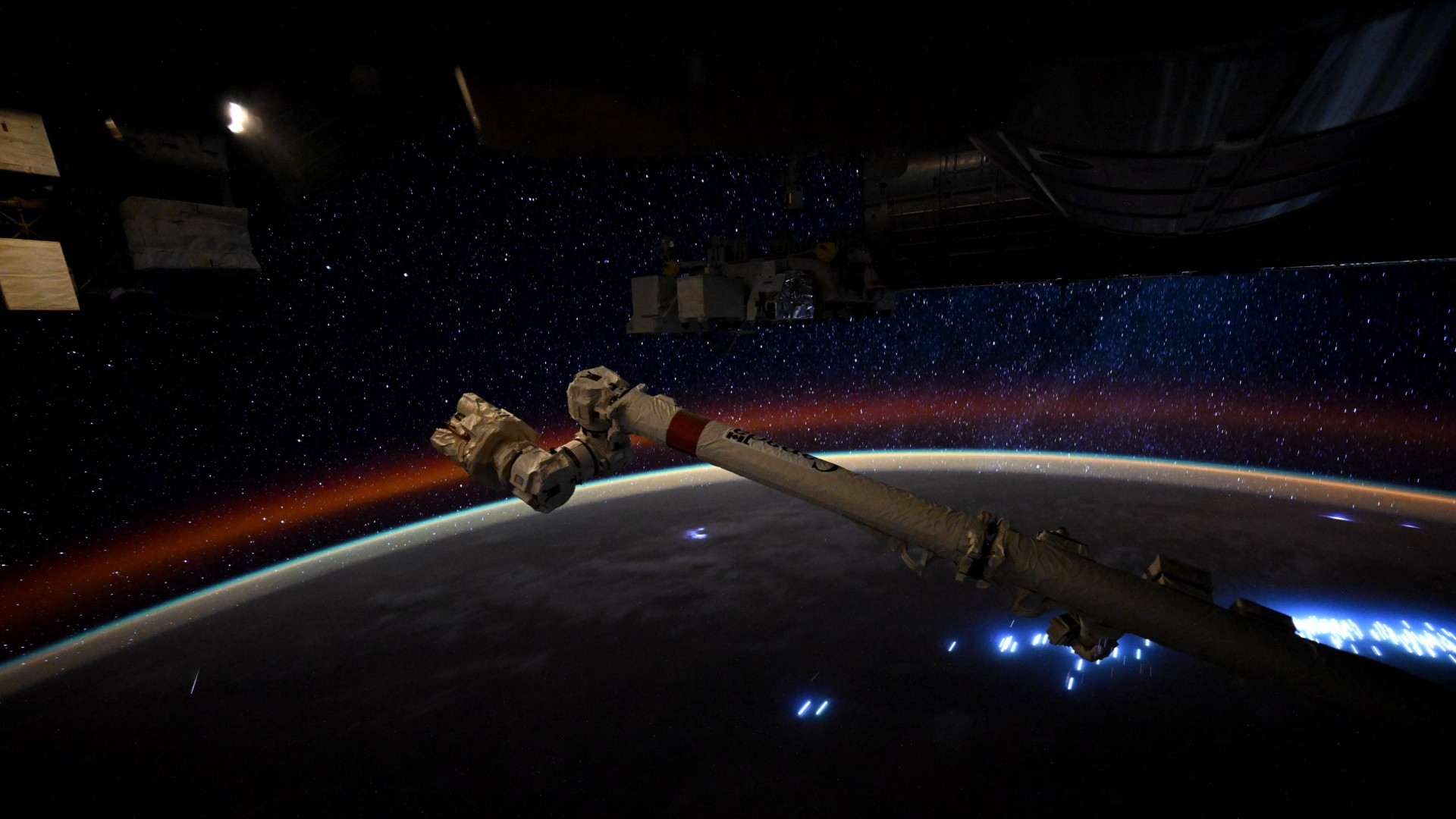 a streak of light crosses a starry sky above a dark earth below it