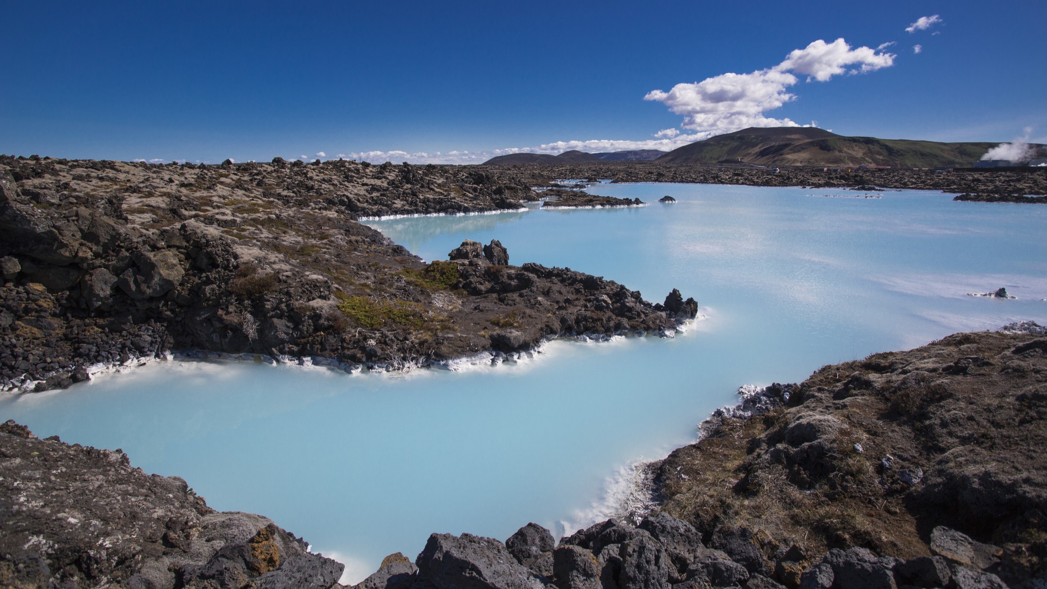 luscious blue water and a blue sky surrounded by contrasting black rocks.