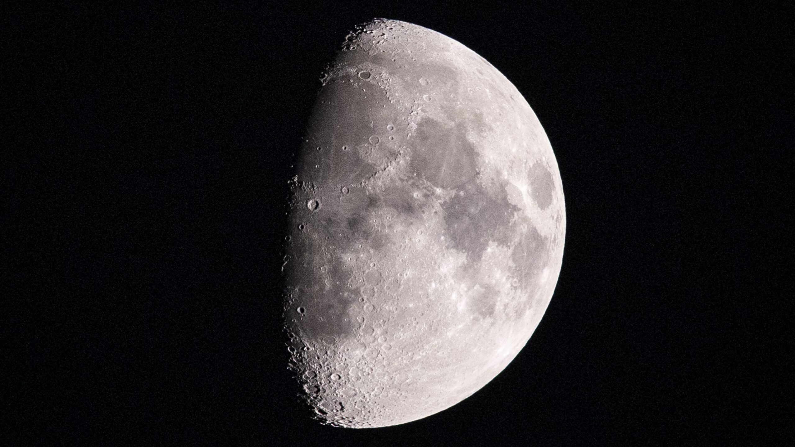 A photo of a waxing gibbous moon shown with its right side lit in a black sky.