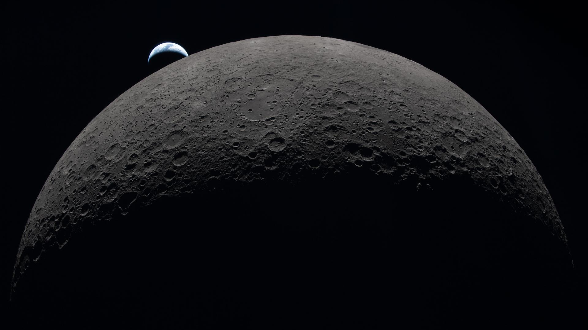 photo from a spacecraft showing a tiny crescent earth hovering above a giant-looking moon
