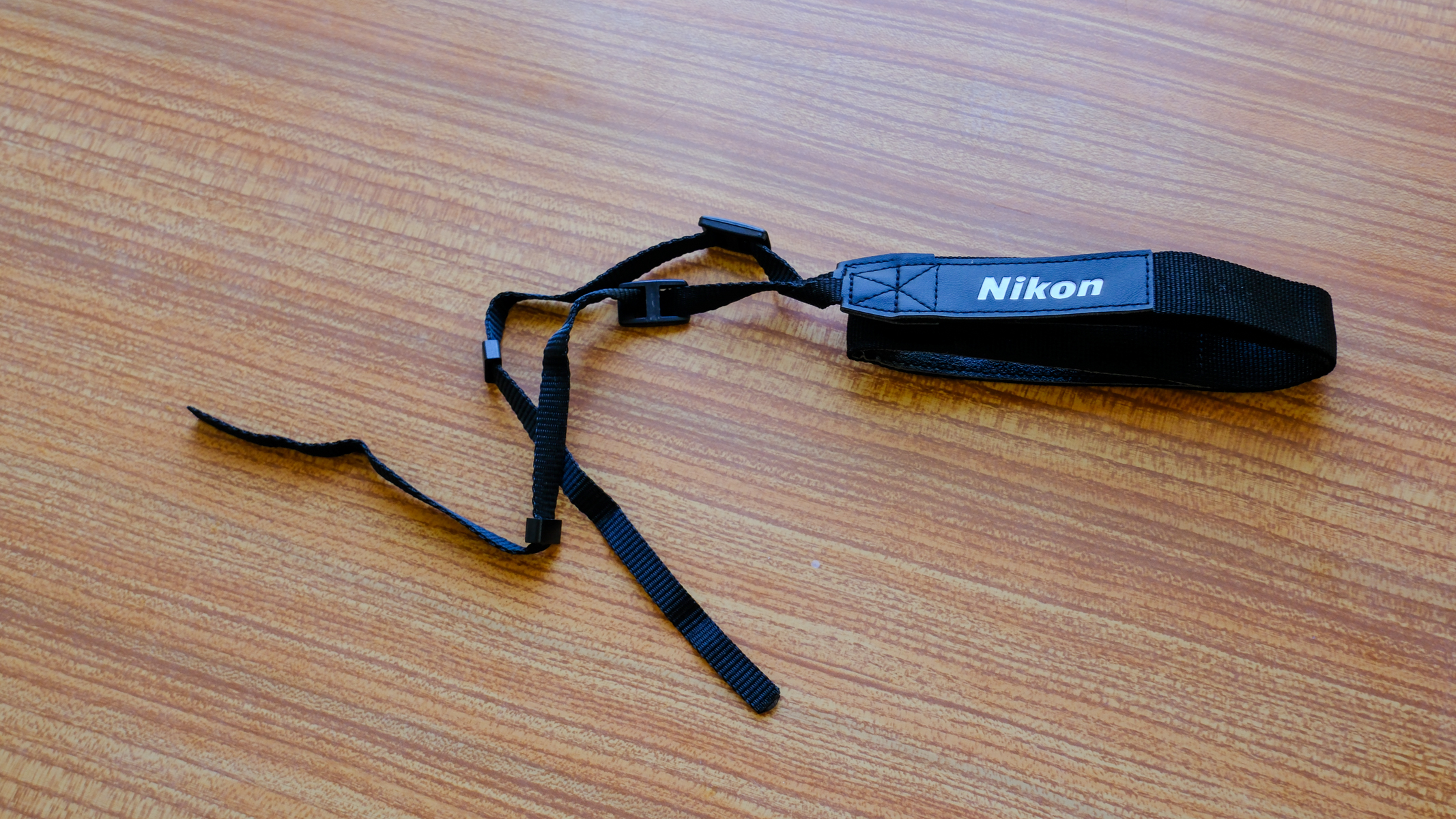 The neckstrap for the Nikon Action 7x50 binoculars on a wooden table.