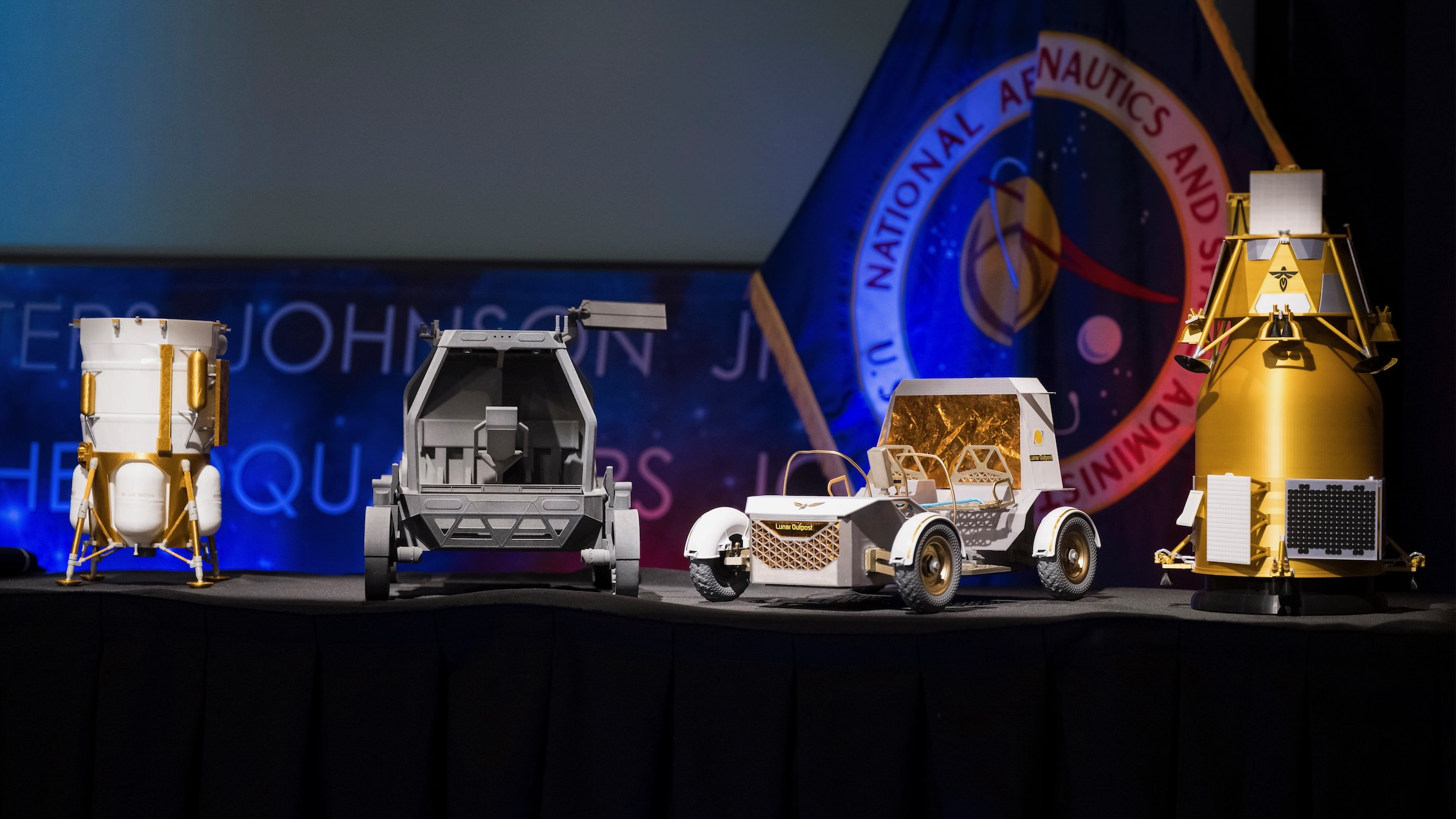 Left to right: Models of the Blue Origin Mk 1 lander, Astrolab Crewed Lunar Rover, Lunar Outpost Pegasus rover and Firely's Elytra Dark orbiter at a May 26, 2026 NASA press briefing.