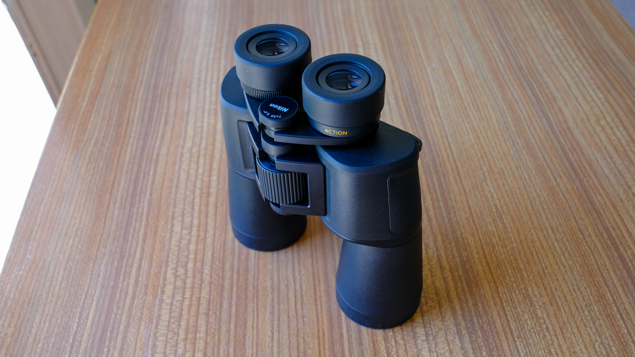 The Nikon Action 7x50 binoculars lens down stood up on a wooden table, with eyecups down.