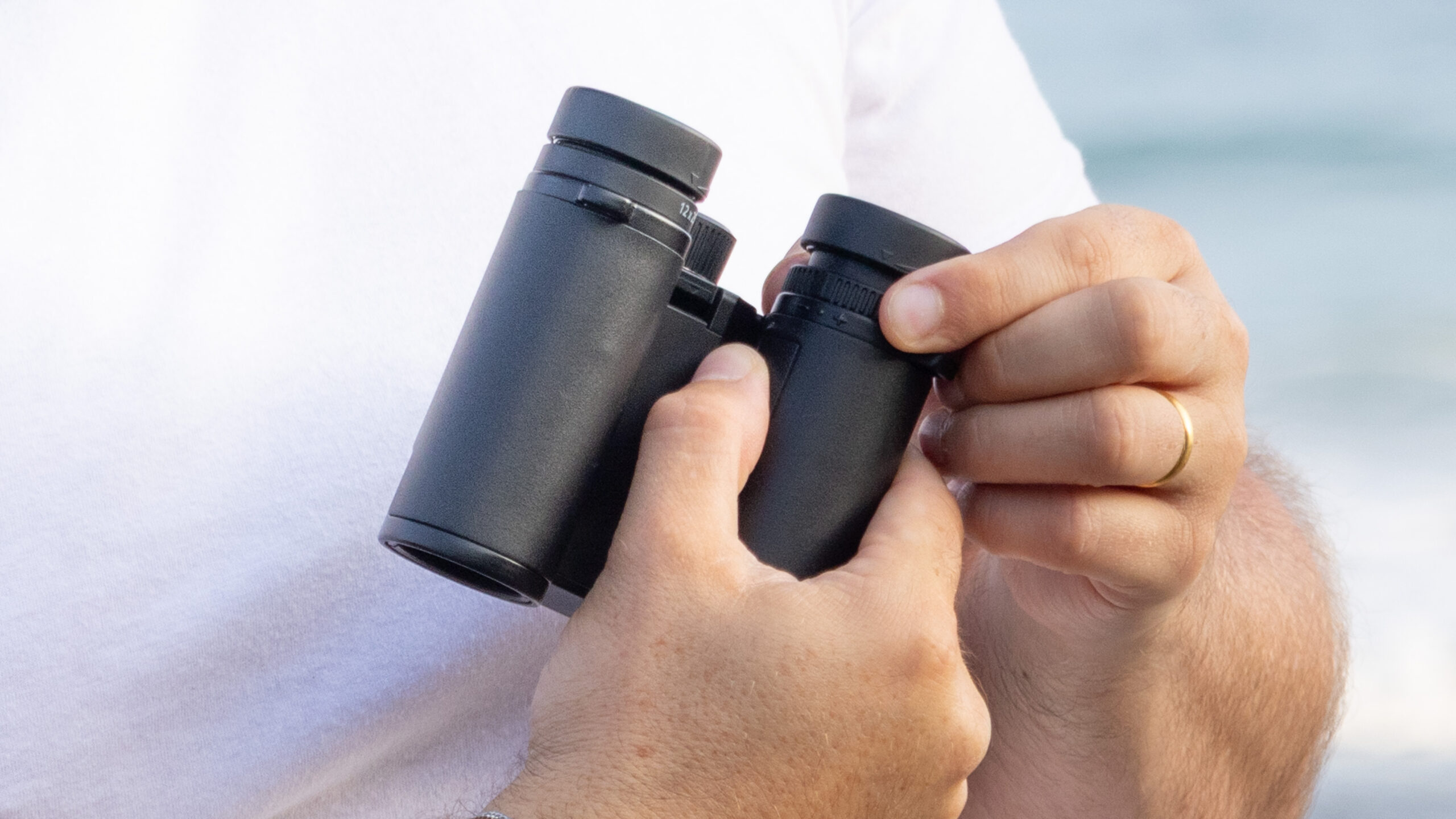 Nikon Stabilized 12x25 S binoculars held in the hands of the reviewer in front of breaking waves at the beach