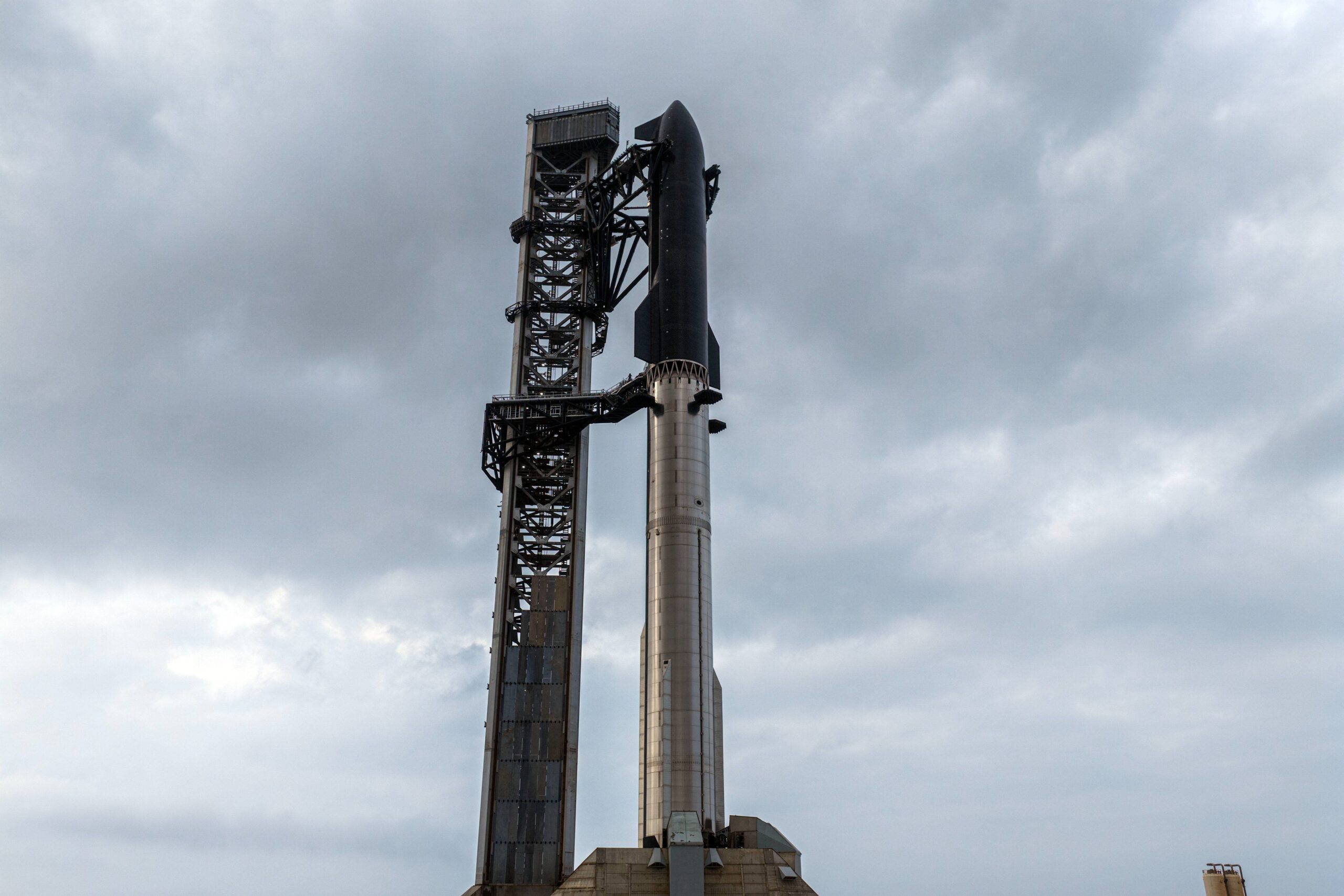 a giant chrome rocket booster and black-tiled spacecraft stand tall on a launchpad next to a gray tower.